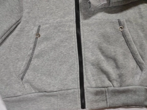 Detail der grauen Sweatjacke mit Reißverschluss, Seitentaschen mit Nieten und Rippsaum