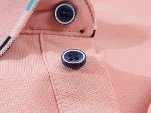 Détail macro du polo en piqué rose avec boutons bleu marine et col à rayures