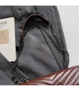 Detail of dark brown V-quilted leather crossbody bag with metal chain strap on suit fabric
