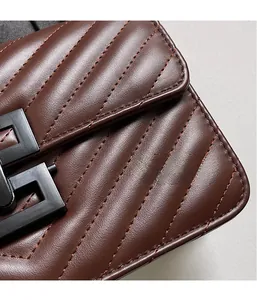 Detail of dark brown leather crossbody bag with chevron stitching and black hardware