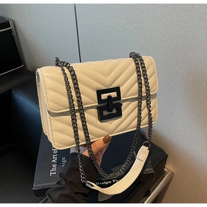 Close-up of cream quilted crossbody bag with stylish black square lock and chain strap