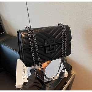 Detail of black quilted chain bag featuring V-shaped stitching and a square metal clasp