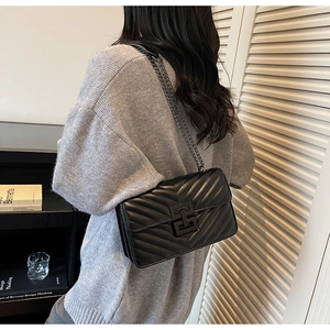 Rear view of a model wearing a black quilted leather shoulder bag with a metal chain strap