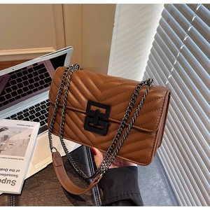 Detailed view of caramel quilted crossbody bag with black metal lock on a desk
