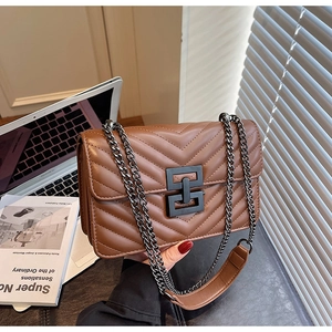 Close-up of brown V-quilted leather texture with matte black chain and geometric buckle