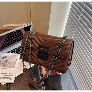 Detail of dark brown quilted crossbody bag with metal chain strap in urban office setting