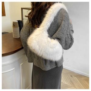 Close-up of a white fluffy faux fur shoulder bag worn over a grey sweater in a cafe setting