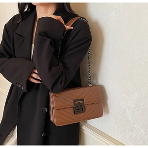 Detail of a brown quilted leather crossbody bag featuring a black metal H-shaped clasp