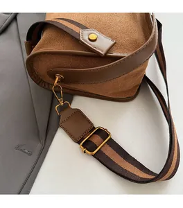 Close-up of brown suede bag with gold hardware and striped woven shoulder strap