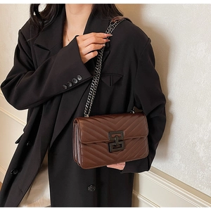 Close-up of brown quilted shoulder bag with chevron stitching and metal chain strap