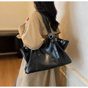 Detail of black leather tote bag featuring silver metal grommets and buckle straps