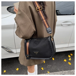 Detail of black Boston bag with wide striped shoulder strap in a stylish street setting