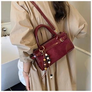 Detail of burgundy crossbody bag with matte texture and vintage beaded tassel charm
