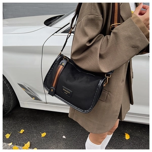 Close-up of black crossbody bag with striped shoulder strap worn on a brown blazer
