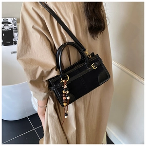 Detail of black glossy baguette bag with gold hardware and colorful beaded charm