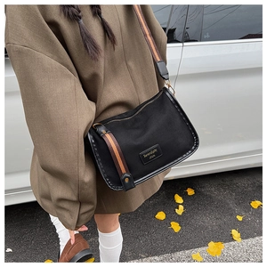 Detail of black canvas crossbody bag with striped strap and Serendipity leather patch