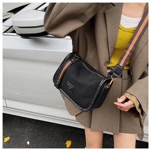 Detail of black suede crossbody bag with wide brown striped strap and logo label