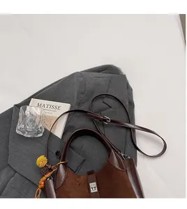 Close-up of brown bucket bag with metal turn-lock and decorative beads on a grey blazer
