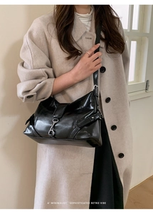 Close-up of black glossy retro shoulder bag with silver hardware on a beige coat