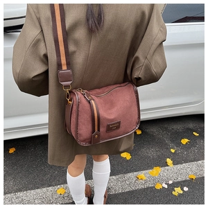 Close-up of burgundy suede square bag with striped canvas strap on female model