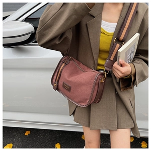 Detailed view of burgundy canvas crossbody bag with striped wide strap and logo patch