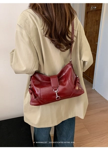 Detail of burgundy leather dumpling bag worn as a shoulder bag in minimalist retro style