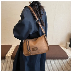 Detail of retro brown crossbody bag featuring wide striped strap and leather logo tag