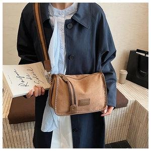 Brown suede crossbody bag with a wide striped shoulder strap shown in a lifestyle scene