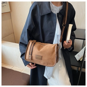 Close-up of brown suede crossbody bag with wide striped strap and Serendipity label