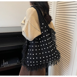 Detail of black knit tote bag with white pearls and decorative fringe edges