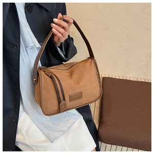 Detail of brown suede shoulder bag with 'Serendipity' embossed leather patch and wide strap