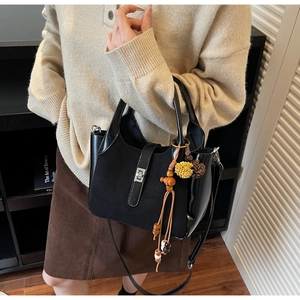 Close-up of black matte and patent leather bucket bag with silver lock and beaded tassel