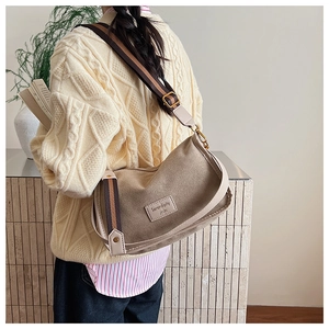Khaki crescent crossbody bag with striped wide strap worn over a beige knit sweater