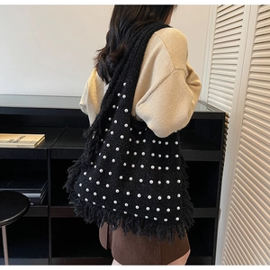 Detail of black knit tote bag with pearl accents and fringe edge on a shoulder strap
