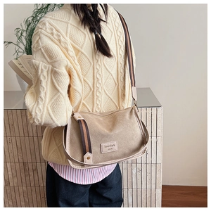 Detail of beige textured crossbody bag with striped webbing strap and brand label