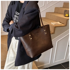 Detail of dark brown leather tote bag with gold HOCDUU logo and reinforced studs