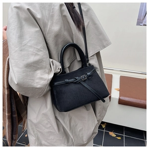 Detail of a black matte suede bucket bag shown in an autumn scene with fallen leaves
