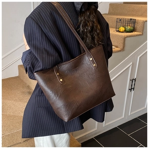 Brown leather tote bag detail with slim shoulder straps and gold rivet accents
