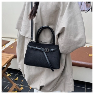 Detail of matte black crossbody bag with faux leather straps and metal buckle accent