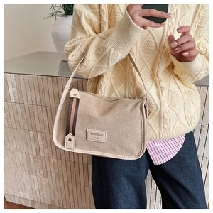 Detailed close-up of beige shoulder bag featuring striped webbing and square logo patch