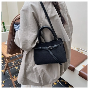 Detail of black suede-style crossbody bag with leather strap and buckle in street setting