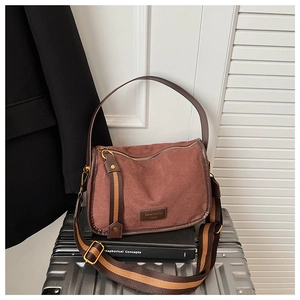 Detail of vintage brown suede crossbody bag with wide canvas strap and brand logo