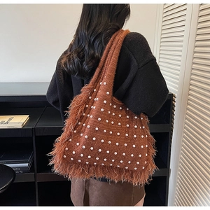 Detail view of brown knit tote bag with pearls and long bohemian fringe on shoulder