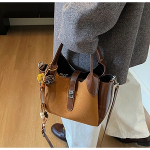 Detailed view of two-tone bucket bag with ethnic charms on warm indoor wooden floor