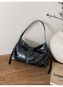 Detail of glossy black leather baguette bag with metal hook on a wooden texture background