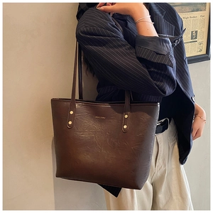 Detail of a dark brown vintage leather tote bag with gold rivets and MOCOMO logo
