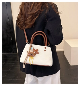 Dettaglio della borsa a secchiello bianca con manici marroni e ciondolo a orso
