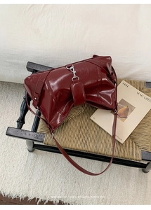 Detailed view of burgundy patent leather crescent bag with silver metallic hook buckle