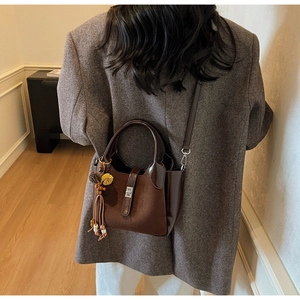 Close-up of brown suede bucket bag with leather trim and decorative beaded tassel charm