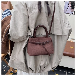 Detail of dark brown matte texture handbag showing round handles and crossbody strap